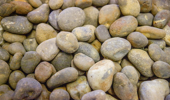 Loose display of rounded roofing shingle, graded from 20mm to 40mm, containing river-washed, multi-coloured pebbles, showcased in a dry condition.