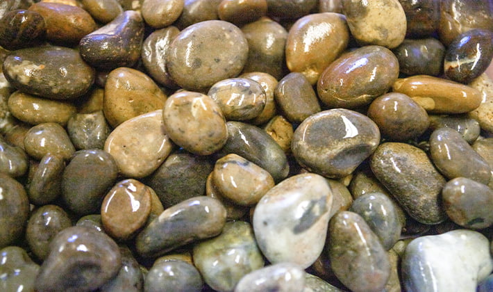 Loose display of rounded roofing shingle, graded from 20mm to 40mm, containing river-washed, multi-coloured pebbles, showcased in a wet condition.